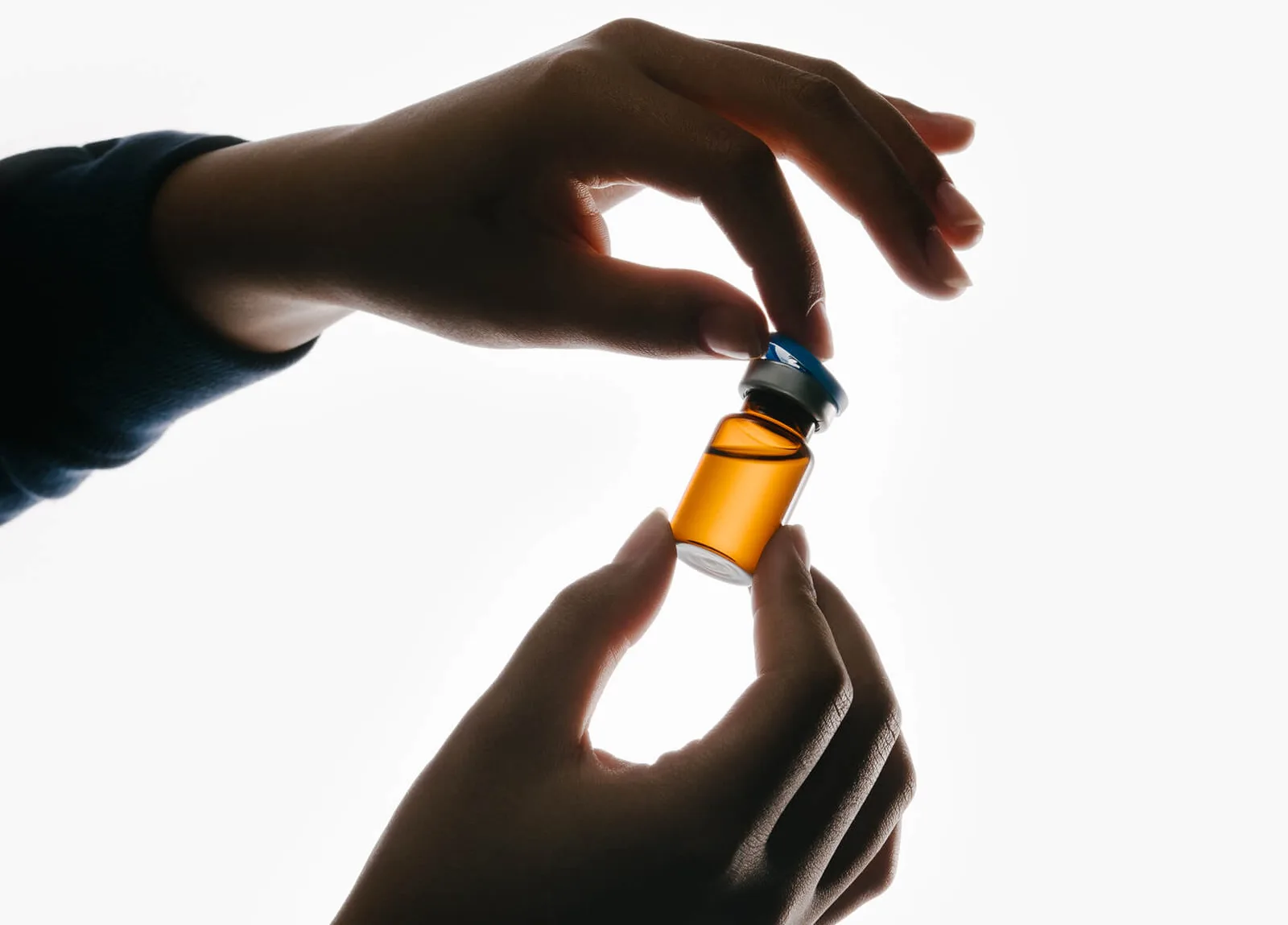 Hands lifting the cap from an amber vial of compounded medication.